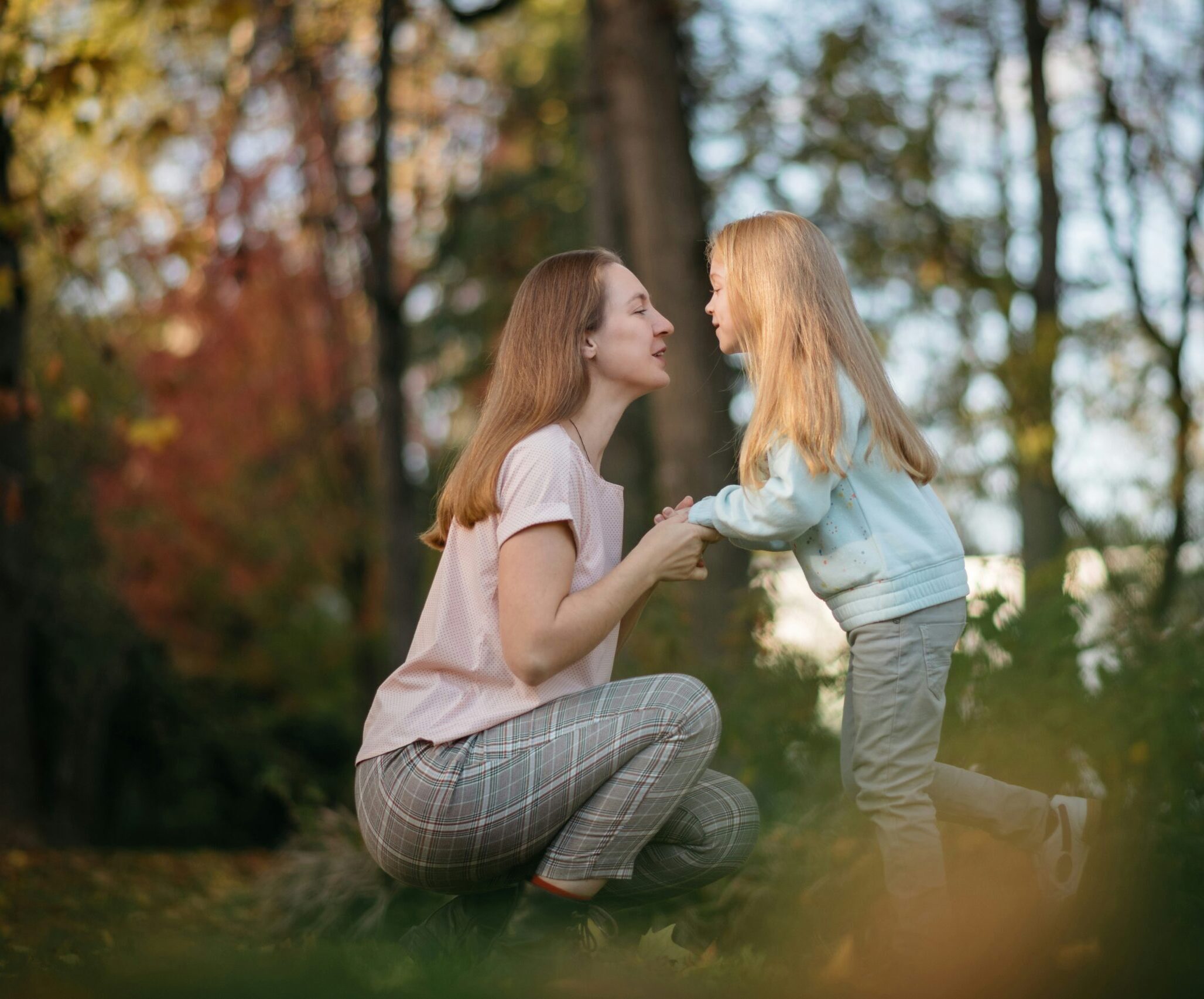 Mother and daughter holding hands and looking at each other in a forest.