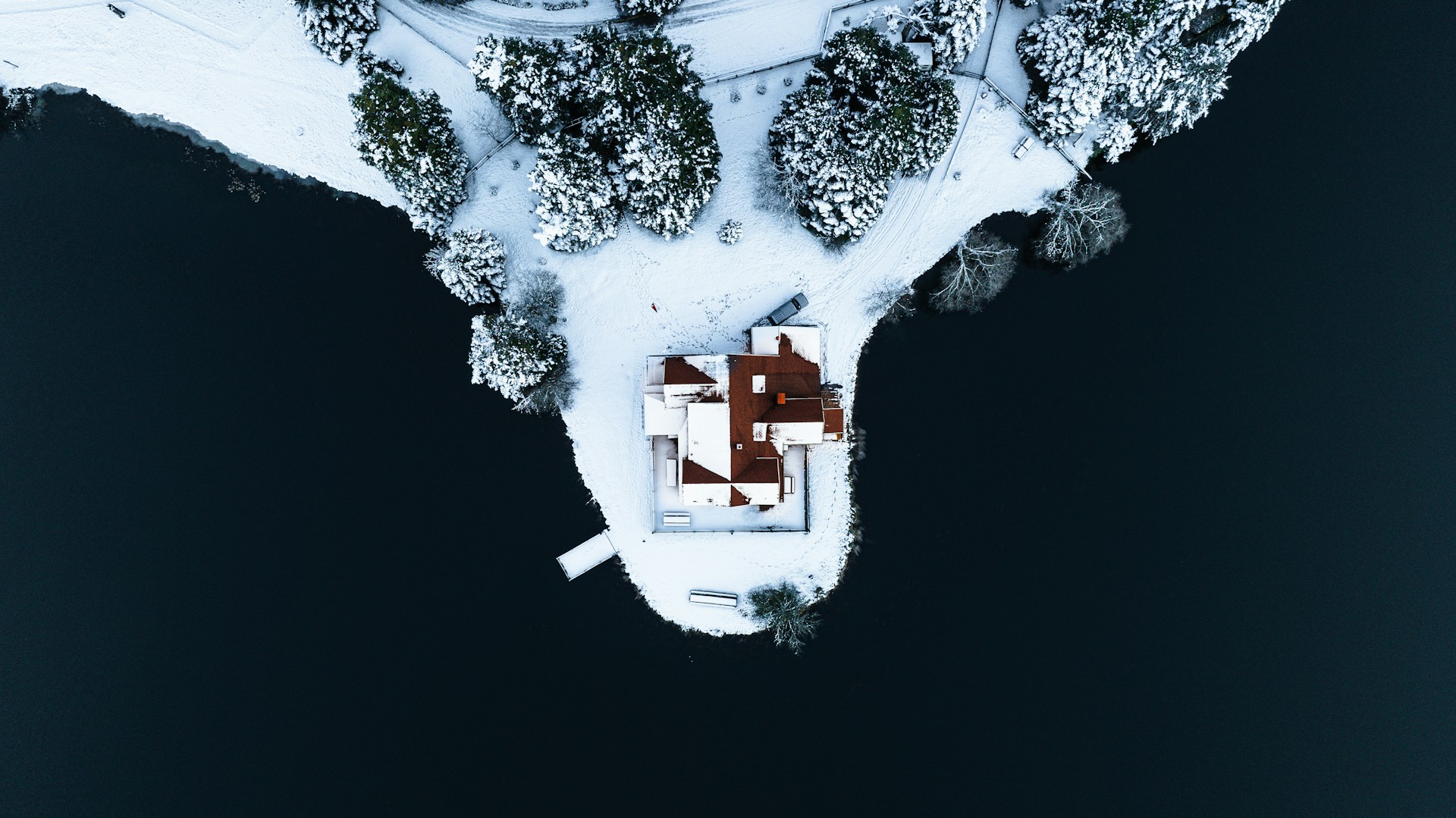 Aerial view of a red-roofed house on a snowy peninsula surrounded by dark water, visually representing a solitary matrimonial home and the complexity of its legal designation and sale under the Family Law Act.