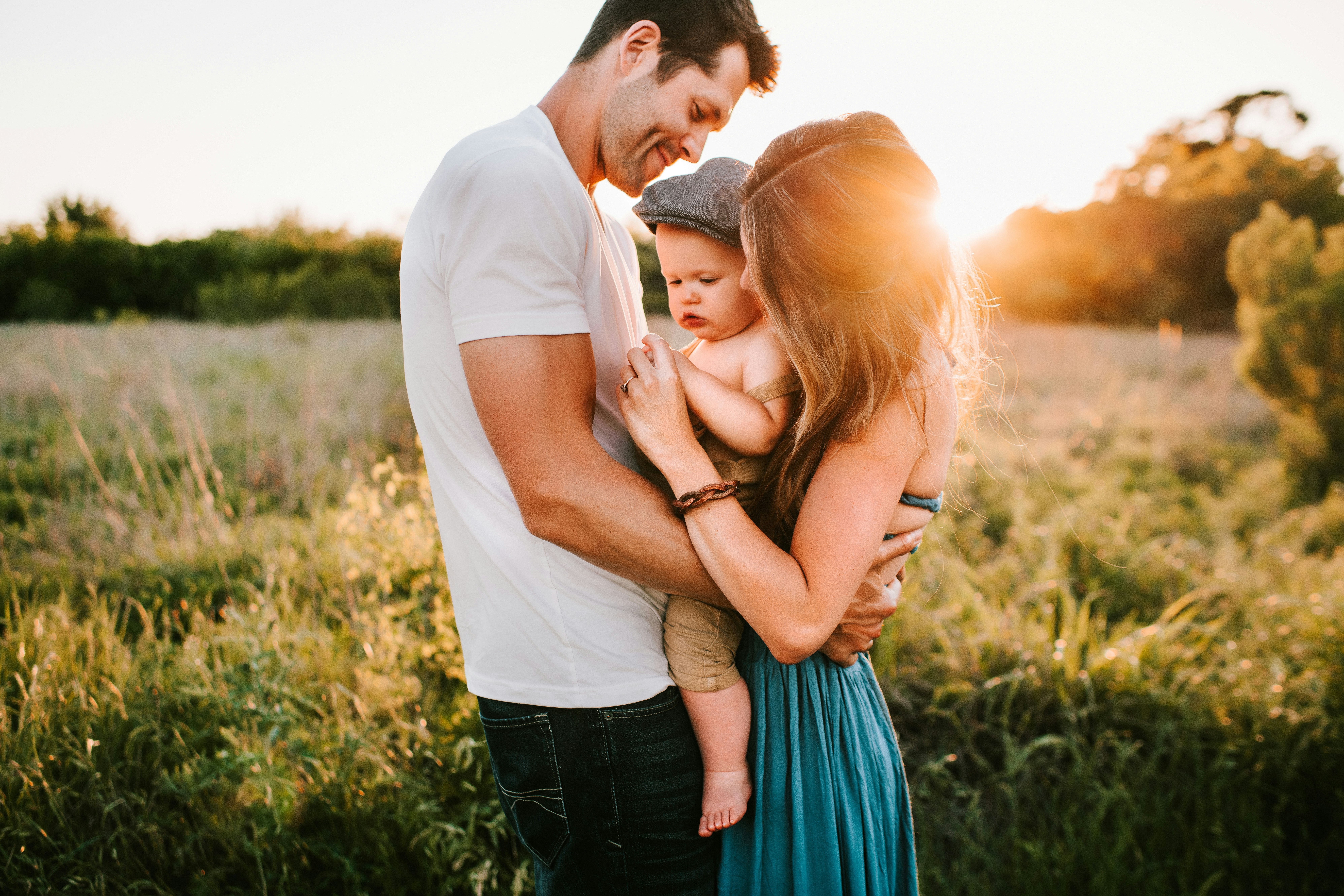 A young couple holding their baby together in a green field during sunset, representing the advice Johnson Millers Family Lawyers provides in child custody/decision-making responsibility and access/parenting time matters in Windsor-Essex.