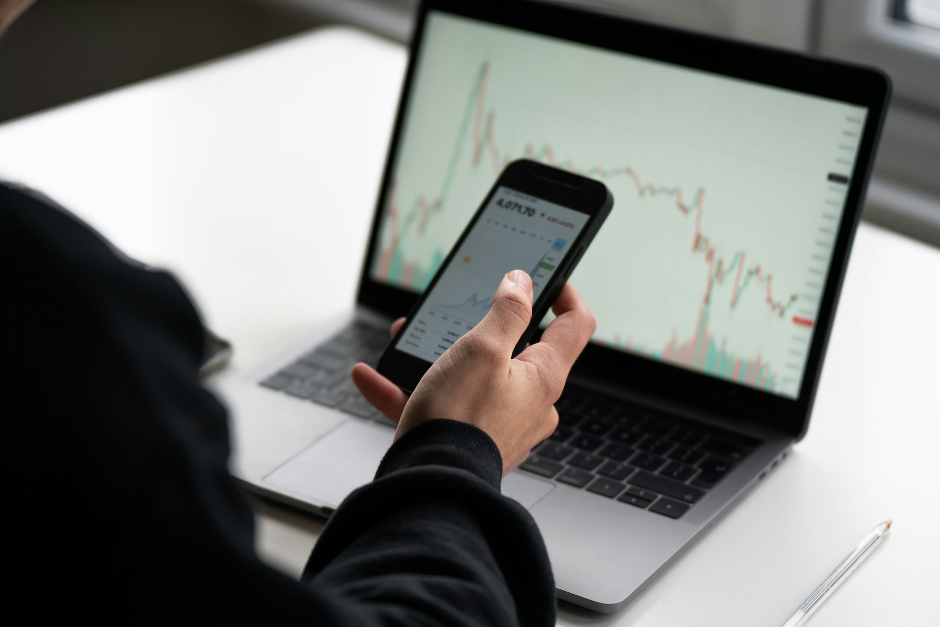 A person holding a phone and looking at a laptop that has stock data displayed, representing stock options and family property division in Divorce.