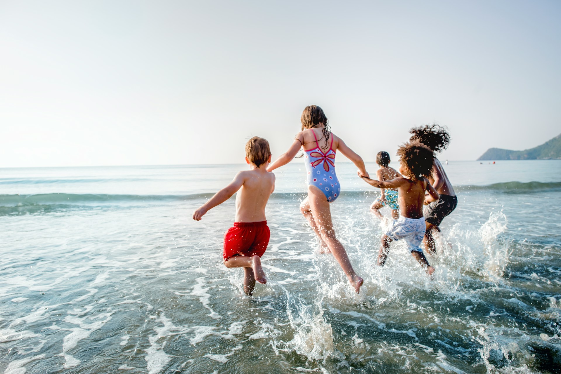 Kids holding hands and running into the water at a beach, representing child support for high-income earners.