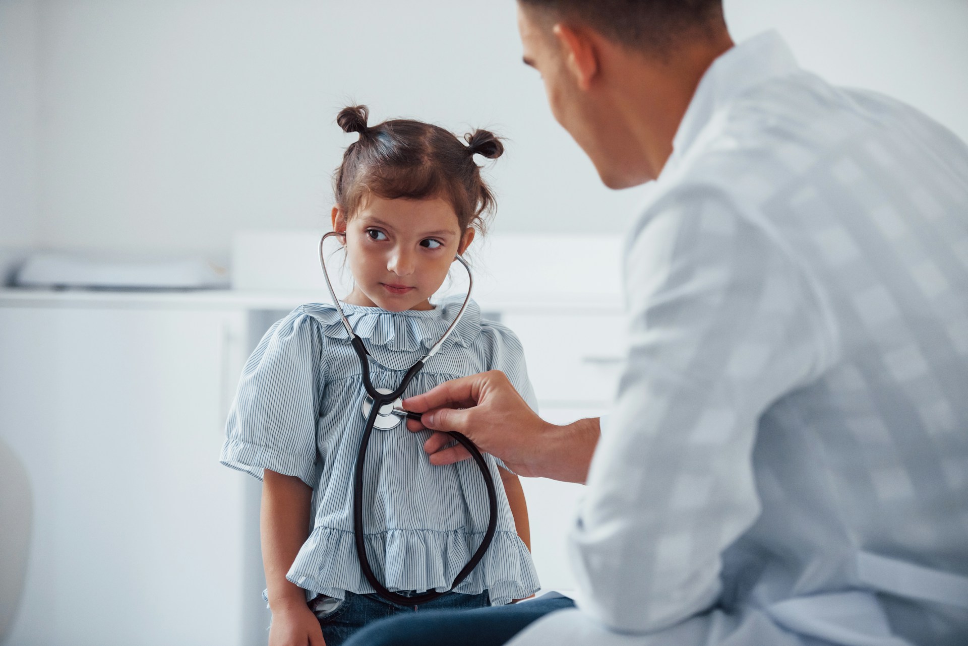 A pediatrician works with a small child holding a stethoscope representing cross-border health costs for children.